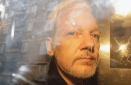 Julian Assange door het venster van zijn transport. Foto: twitter/Caitlin Johnstone 