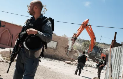 Een Israëlische soldaat met een oorlogswapen staat voor een bulldozer die een huis aan het vernietigen is. Bron: FairFin