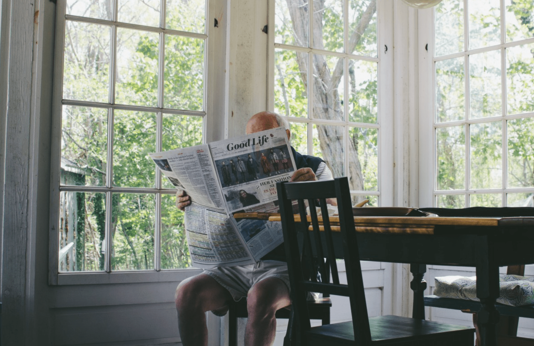 Oudere man leest de krant in zijn huis.