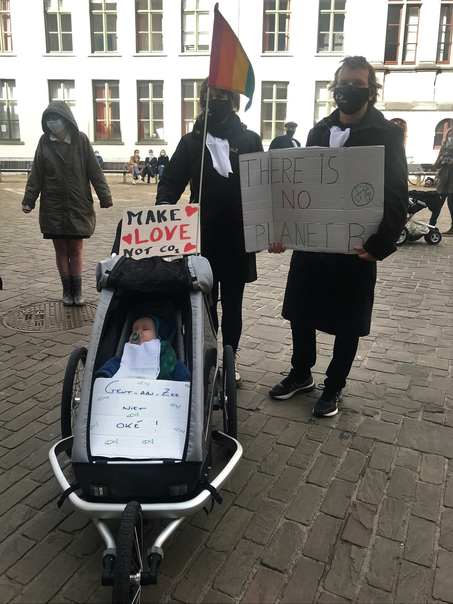 gezin met kinderwagen, protestborden en regenboogvlag
